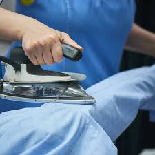 Close-up of hands using steam iron on blue garment showing professional ironing technique at Tooting laundry service